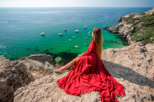 Woman red dress sea. Happy woman in a red dress and white bikini sitting on a rocky outcrop, gazing out at the sea with boats and yachts in the background