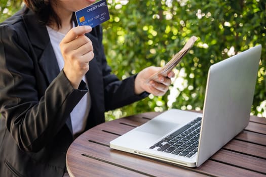 Woman using working and shopping outdoor at cafe coffee shop, Online e-commerce, internet banking, Hands of businesswoman holding thai money and credit card on laptop computer, technology finance