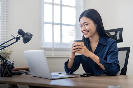 Smiling woman sitting at her desk in office and coffee. Happy business woman sitting in office.