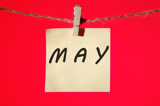 MAY text on a yellow sticker hanging on a rope with clothespins on a red background