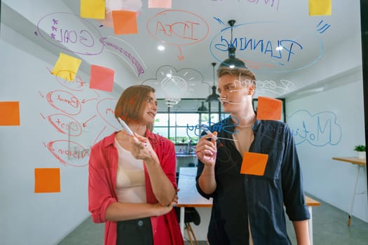 Couple of young creative start up business people brainstorming idea and solving problems by using sticky note and mind map at glass board, meeting room. discussing, working together. Immaculate.