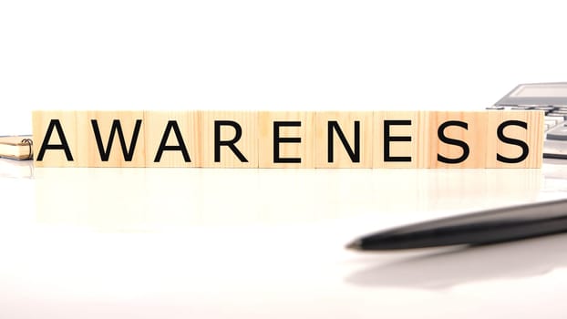 AWARENESS word word assembled from wooden cubes next to a calculator, pen and notepad