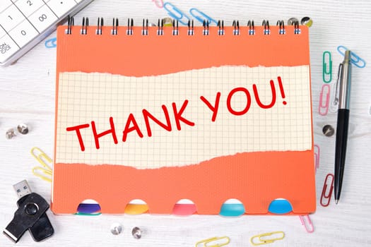 Thank you word is written on a sheet in a cage lying on a notebook on the table next to stationery