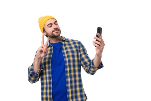 handsome young hipster man in cap and shirt taking selfie on phone on white background with copy space.