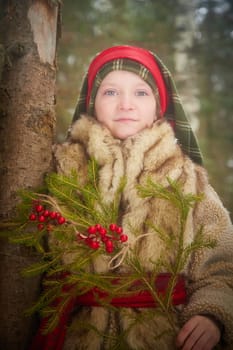 Portrait of Teen girl in coat, red sash and branch of fir tree with bright berries in cold winter day in forest. Medieval peasant girl with firewood. Photoshoot in stile of Christmas fairy tale