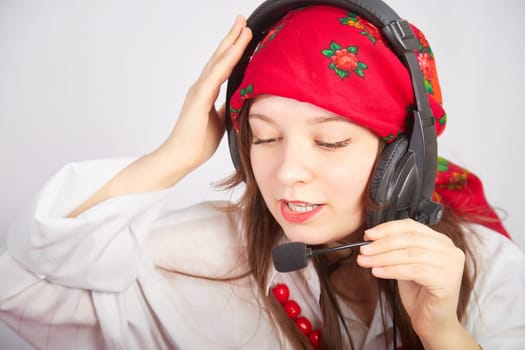 Portrait of young girl in a bright red scarf and large headphones with a microphone. A woman who is radio or television presenter in the workplace. Funny female telecom operator. Freelancer at work