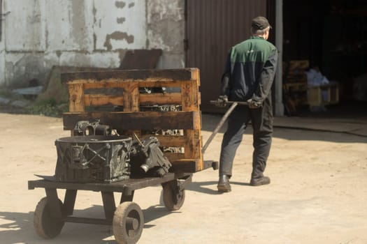 Man carries cart. Worker pulls load. Forklift on street. Man drags vehicle.