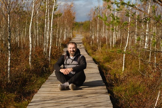 A man sits on a wooden path in a swamp in Yelnya, Belarus.