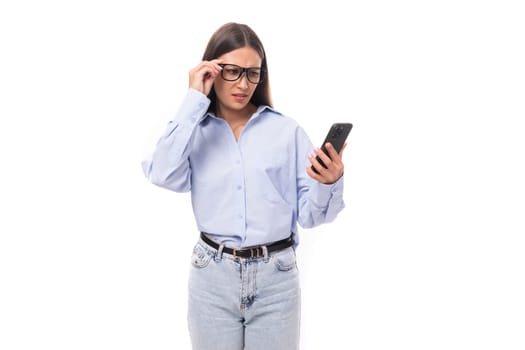 young pretty european brunette business woman with light makeup in a light blue blouse uses a smartphone to solve work issues.
