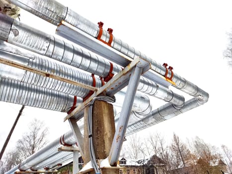 Metal pipes in thermal insulation winding outdoors and the over-illuminated white sky on background