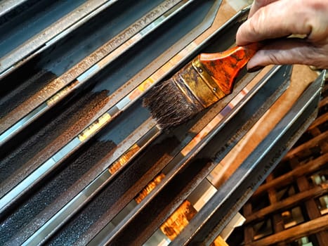 A brush in woman's hand paints iron metal bars with brown paint. Work and worker