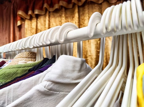 Hangers with a variety of clothes on white rack. Home storage of clothes. Clutter. Littery. Declutter. Garage sale