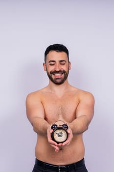 Middle-aged white man looks on an alarm clock in hand on grey background, copy space for text