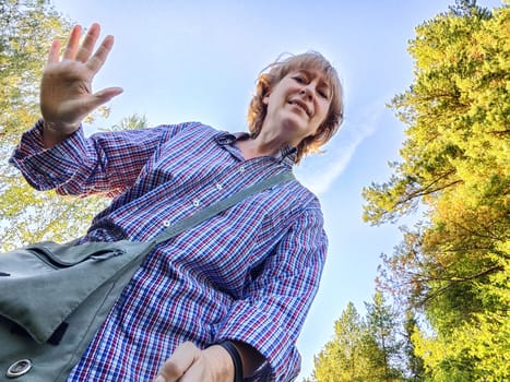 Funny adult girl posing in nature and blue sky on background. A middle-aged woman takes a selfie in the landscape. City tourist on vacation on picnic