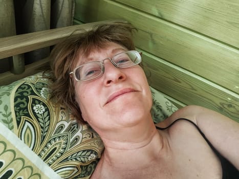 A shaggy, funny middle-aged woman in glasses takes selfie on her smartphone in the bed in early morning. A blogger girl with disheveled hair takes pictures of herself for a blog. Daily routine