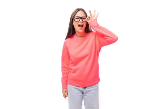 pretty joyful young brunette caucasian woman with straight hair is dressed in a pink sweatshirt and jeans on a white background with copy space.