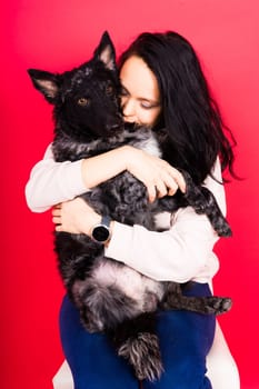 Happy brunette lady in a casual wear hugging mudi pet dog, studio background.