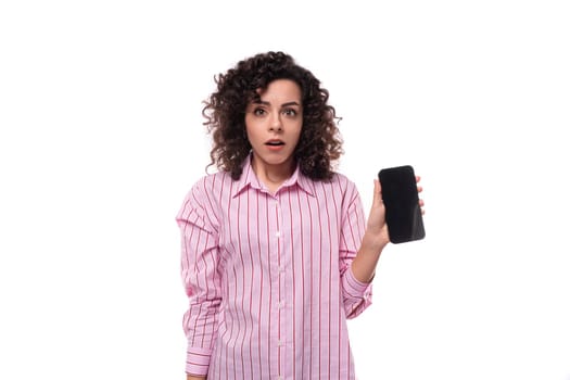 portrait of a surprised 30 year old slim curly brunette woman model dressed in a pink shirt with a smartphone in her hands. e-business concept.