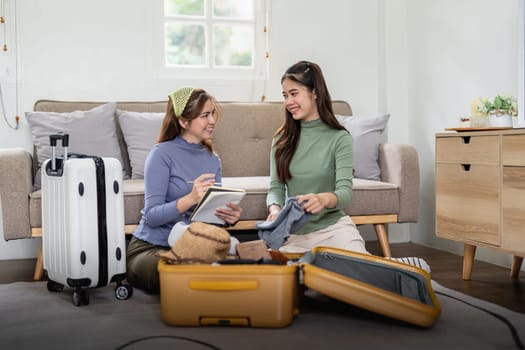 Asian beautiful tourists two women friend help collect clothes and supplies. Young female traveler feeling happy and enjoy, prepare luggage and ready for holidays vacation trip together.