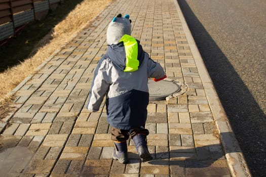 Child runs down road. Boy on street. Warm clothes on baby. Walk on windy day.