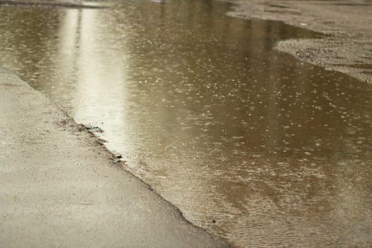 Rain outside. Large puddle in yard. Wet weather. Surface of puddle. Water on road.