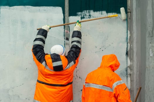 Workers paint wall. Wall flogging. Orange clothing of workers. Smearing graffiti. Fight against vandalism.