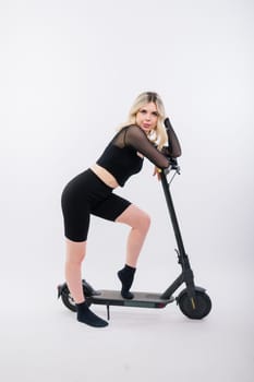 Beautiful emotional young female in a sport clothes on electric scooter on red and white background