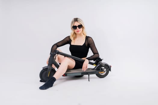 Beautiful emotional young female in a sport clothes on electric scooter on red and white background