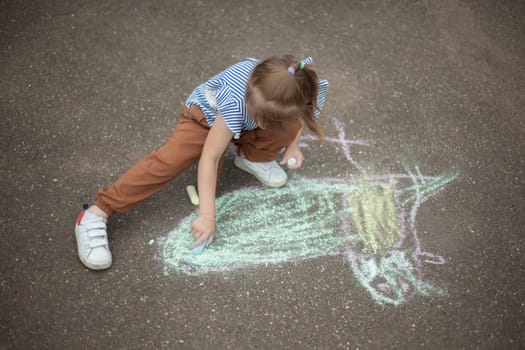 Child draws on asphalt with chalk. Child plays outside. Creative abilities of baby. Girl artist.