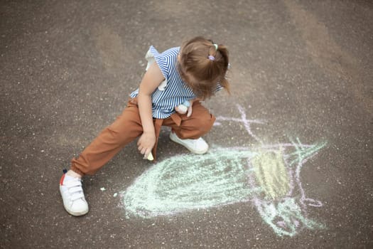 Child draws on asphalt with chalk. Child plays outside. Creative abilities of baby. Girl artist.