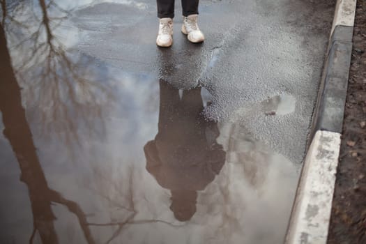 Reflection of person in puddle. Puddle outside. Person stands on wet road. Feet on asphalt.