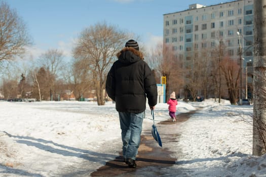 Man goes after child. Man in black jacket. Unknown person on street. Father and child walk in winter.