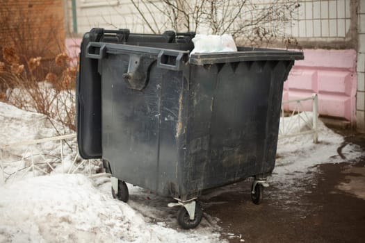 Black garbage can on street. Dirty container in ghetto. Waste garbage. Container on wheels.