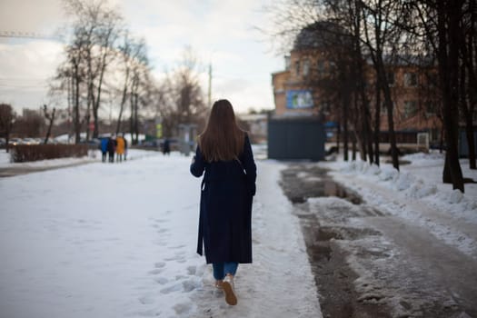 Girl walks down street in winter. Woman in winter in city. Bad road in yard in Russia. Student returns home.