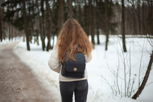 Girl walks down street in winter. Woman in winter in city. Bad road in yard in Russia. Student returns home.