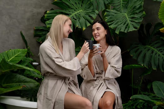 Tropical and exotic spa garden with bathtub in modern hotel or resort with young two women in bathrobe drink coffee, enjoy leisure and wellness lifestyle surround by lush greenery foliage. Blithe