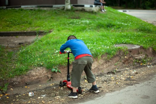 Child on scooter in summer. Boy playing alone. Schoolboy on vacation. Active teenager on street.