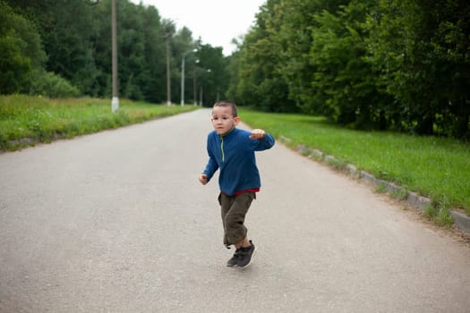 Child runs down road. Boy in summer. Schoolboy on street. Street boy in town.