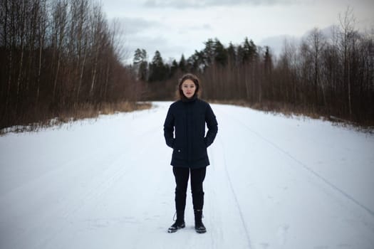 Girl alone on road in winter. Black clothes on cold day. Girl without hat in cold.