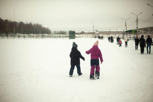 Children walk through snowy field. Children walk outside in winter. Warm clothes in cold weather. Walk down street.