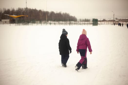 Children walk through snowy field. Children walk outside in winter. Warm clothes in cold weather. Walk down street.