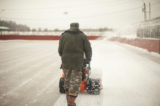 Snow removal at ice rink. Removal of layer of snow from ice. Worker cleans stadium of precipitation. Car is snow grinding.