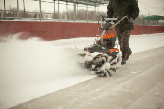 Snow removal at ice rink. Removal of layer of snow from ice. Worker cleans stadium of precipitation. Car is snow grinding.