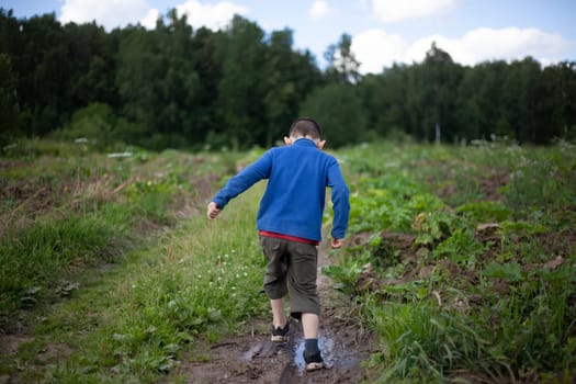 Child walks by nature. Schoolboy walks alone in summer. Boy in blue jacket on street. Lost preschooler.