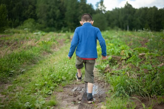 Child walks in mud. Boy trampling on puddle. Schoolboy plays with water. Blue blouse. Bully hits dirt.