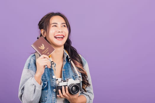 Happy Asian portrait beautiful young woman excited smiling in summer vacation holding passport and vintage photo camera, Thai female ready travel trip looking side away isolated on purple background