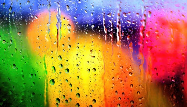 Closeup through window of rainy day with water dripping down glass against blurred