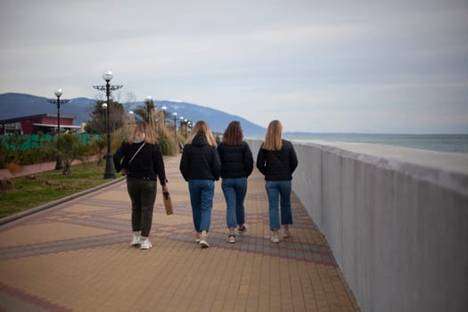 Young girls walk along the arranged promenade by the sea. Friends walk along the stone promenade. Shooting teenagers from the back. Youth today.