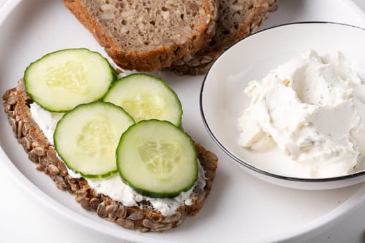 Rye bread with cream cheese and cucumbers on a white table. Whole grain rye bread with seeds.