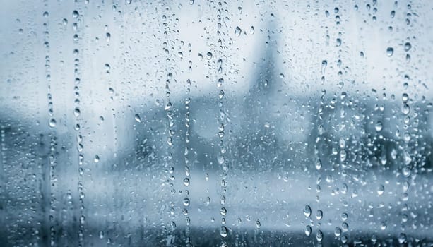 Closeup through window of rainy day with water dripping down glass against blurred